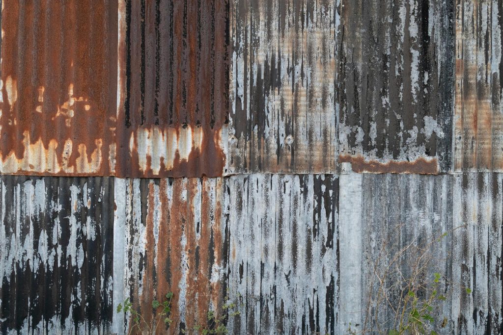 A close-up of a rusty corrugated metal wall with peeling paint, showcasing decay.
