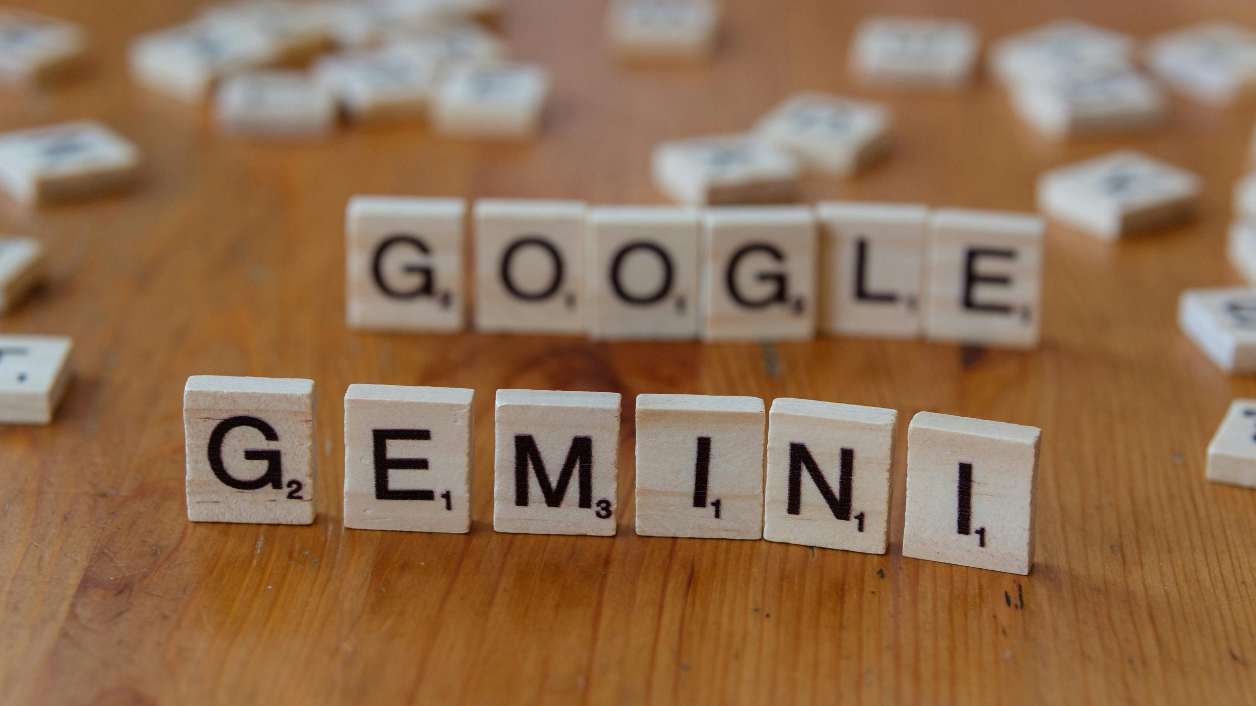 Scrabble tiles spelling out Google and Gemini on a wooden table, focusing on AI concepts.